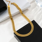Collier torsade dorée en acier inoxydable, maille tissée multi-rangs, posé sur socle noir et blanc