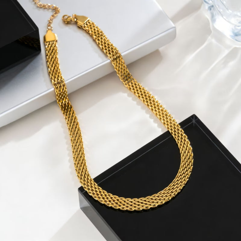Collier torsade dorée en acier inoxydable, maille tissée multi-rangs, posé sur socle noir et blanc