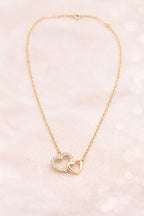 Collier amour femme duo cœur doré serti de pierres sur fond clair beige – bijou romantique pour les amoureux