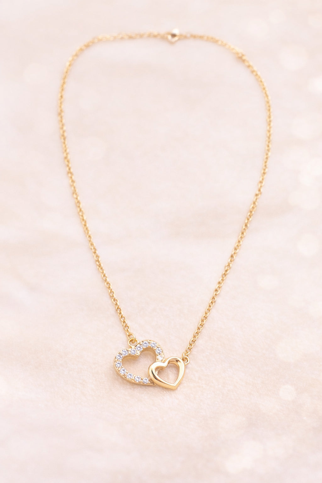 Collier amour femme duo cœur doré serti de pierres sur fond clair beige – bijou romantique pour les amoureux