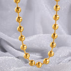 Collier chaîne à perles dorées porté en U sur fond satiné gris - bijou femme minimaliste
