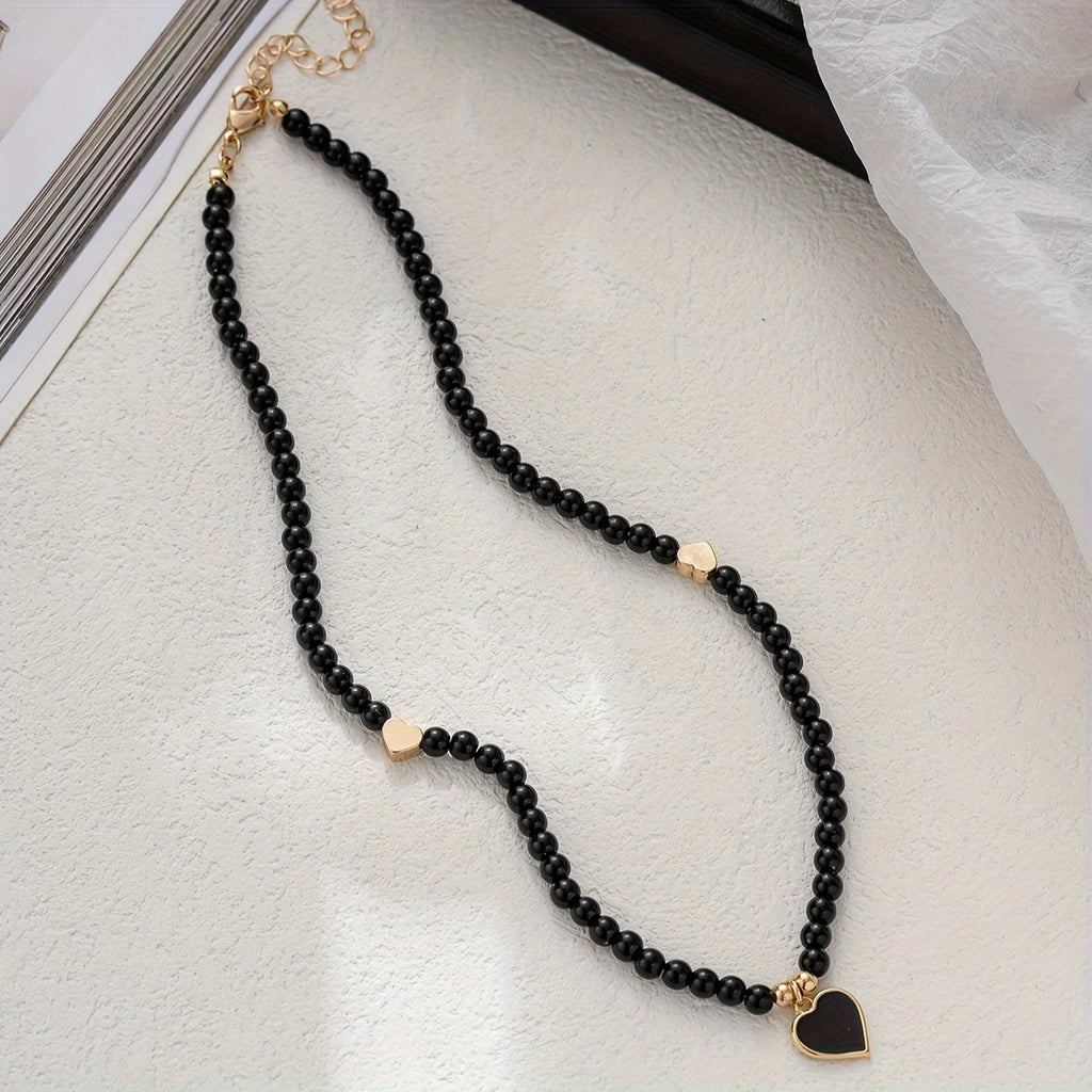 Détail pendentif cœur doré émaillé noir sur collier perles — bijou femme élégant